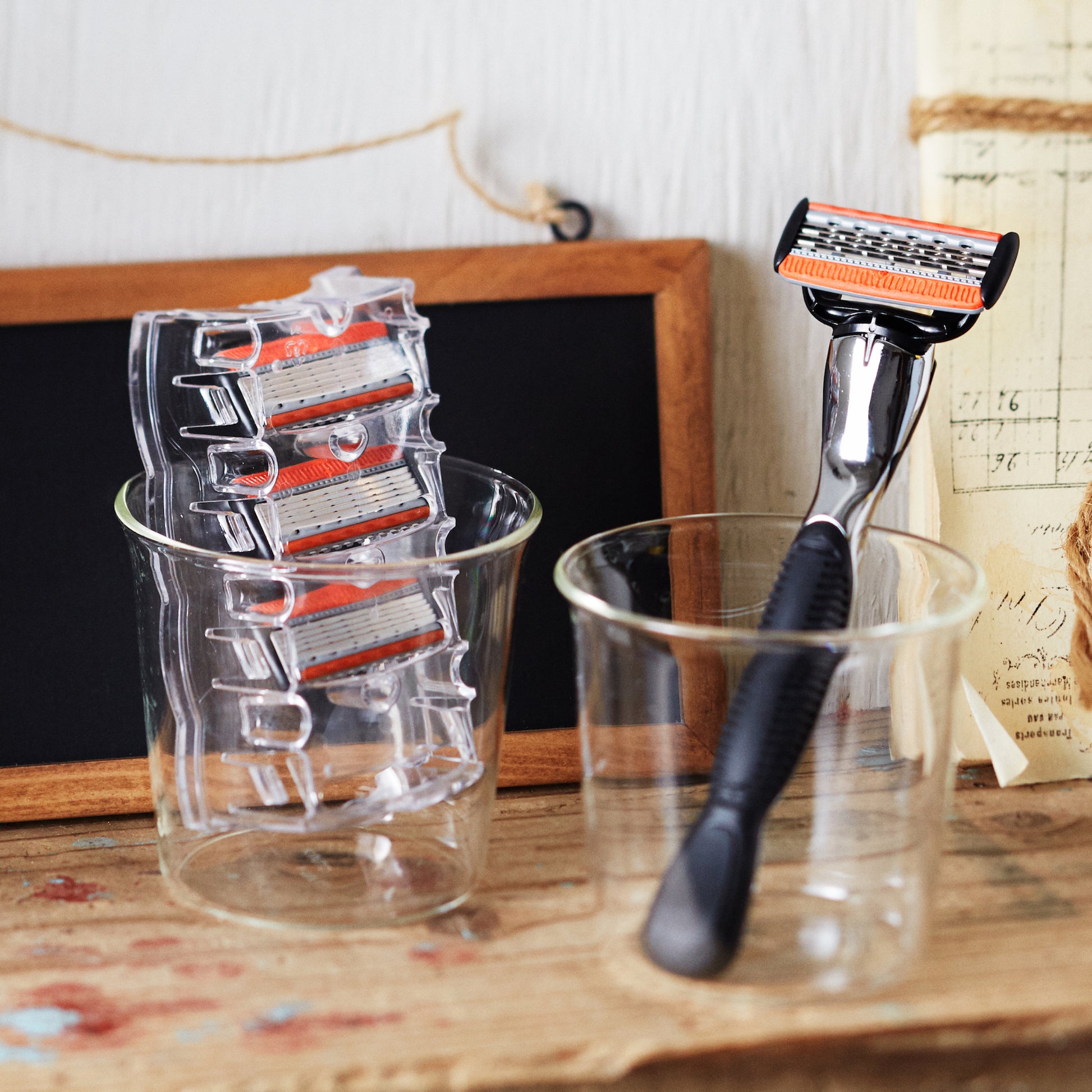 GALLEIDO orange and black razor in a glass cup with replaceable blades in another cup